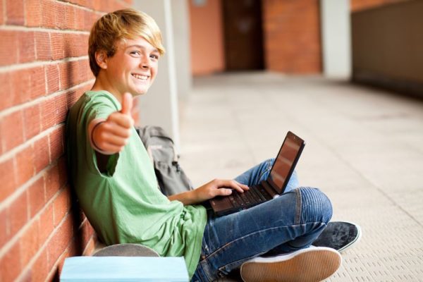 teenage student giving thumb up while using laptop