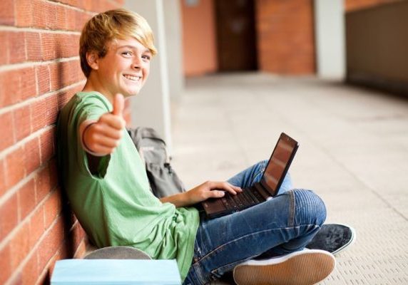 teenage student giving thumb up while using laptop